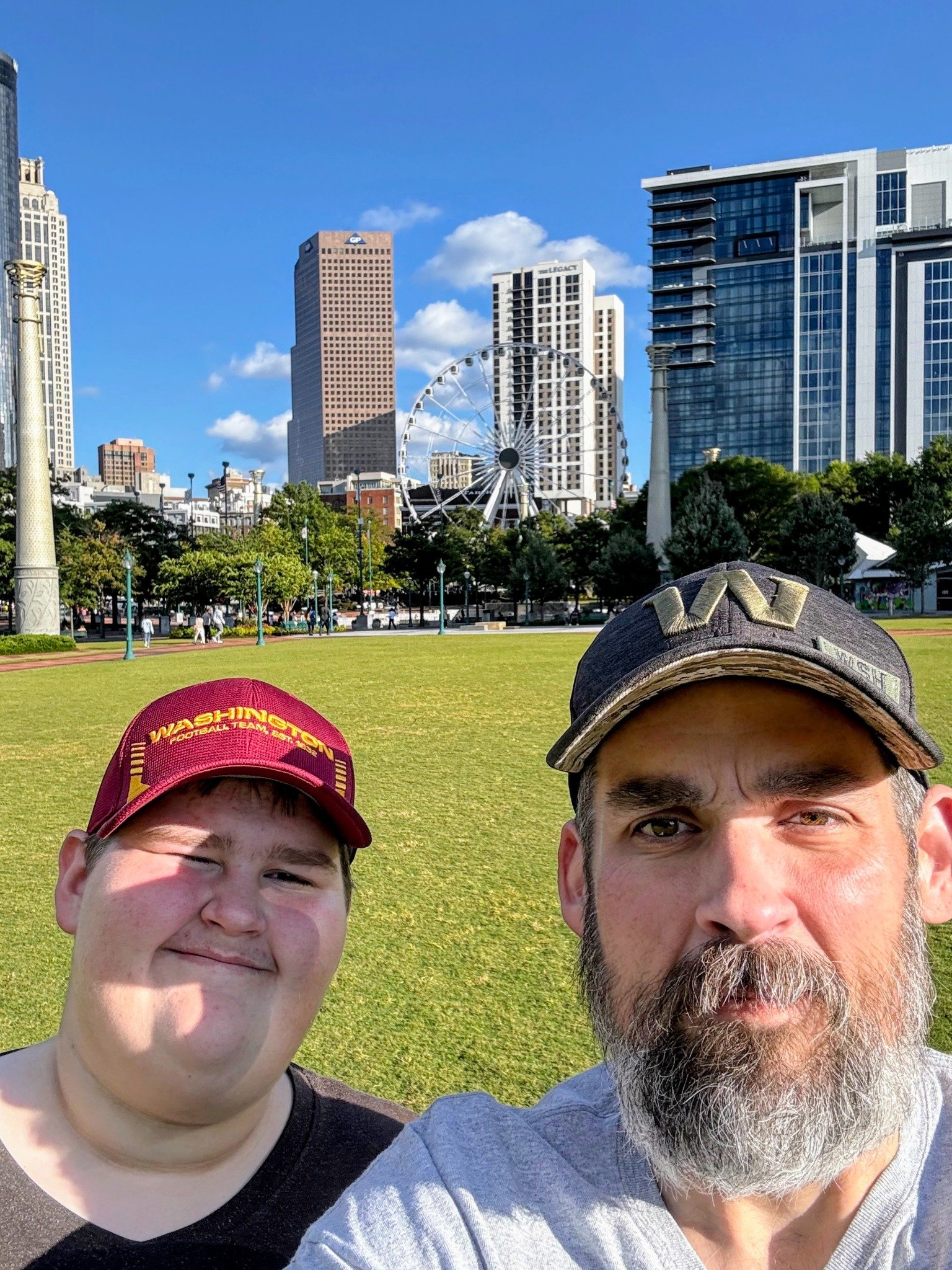 The father and son founders of FrameXR, Greg and Bryant Thomas, smiling in a park with the Atlanta skyline in the background.